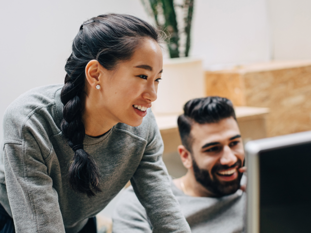 Three colleagues smiling as they look at a computer monitor